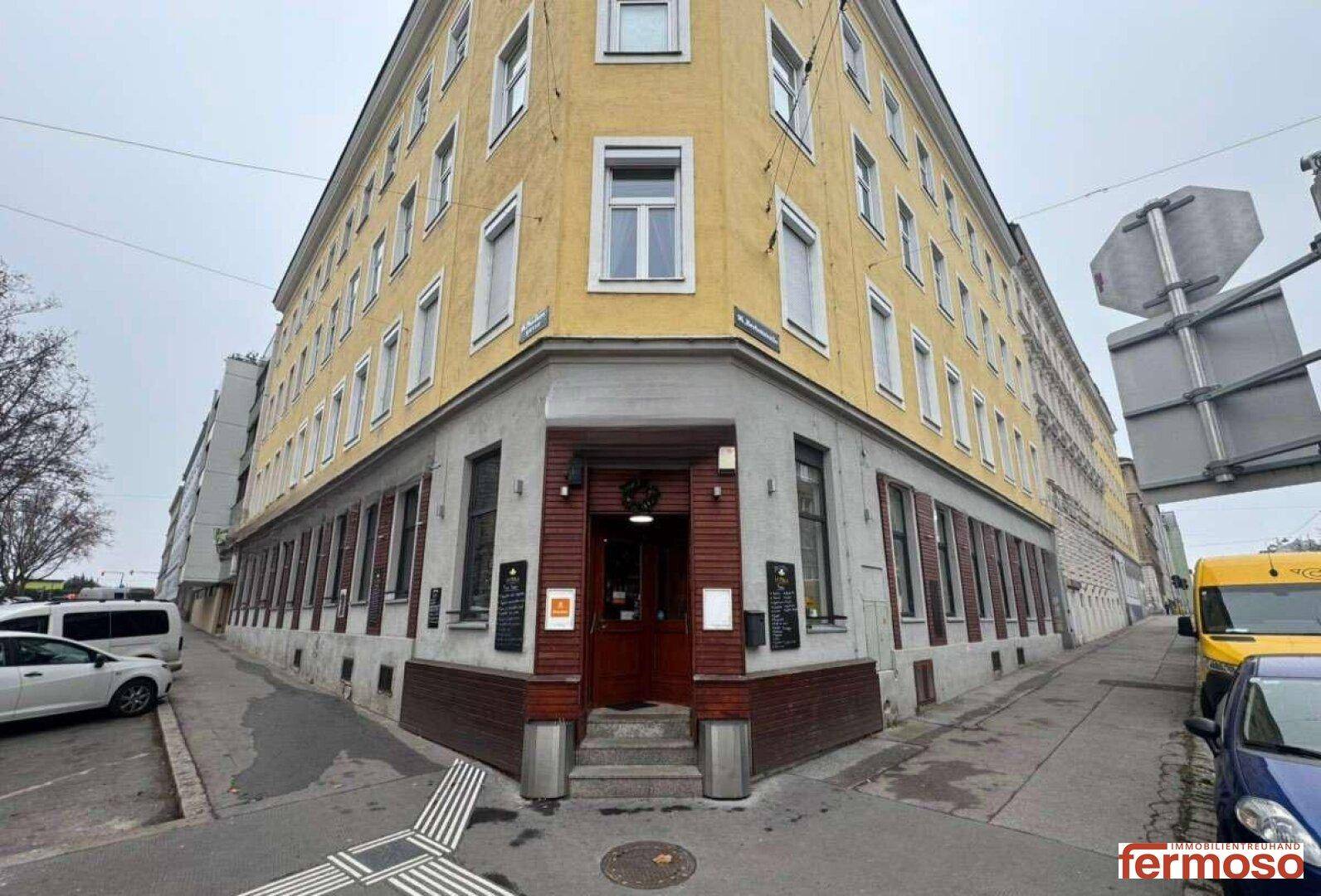 Eckgebäude mit gelber Fassade und einem einladenden Eingangsbereich an der Straßenecke.