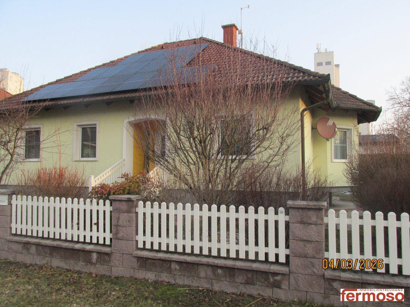 Einfamilienhaus mit Solaranlage auf dem Dach und gepflegtem Vorgarten, umgeben von einer Hecke.