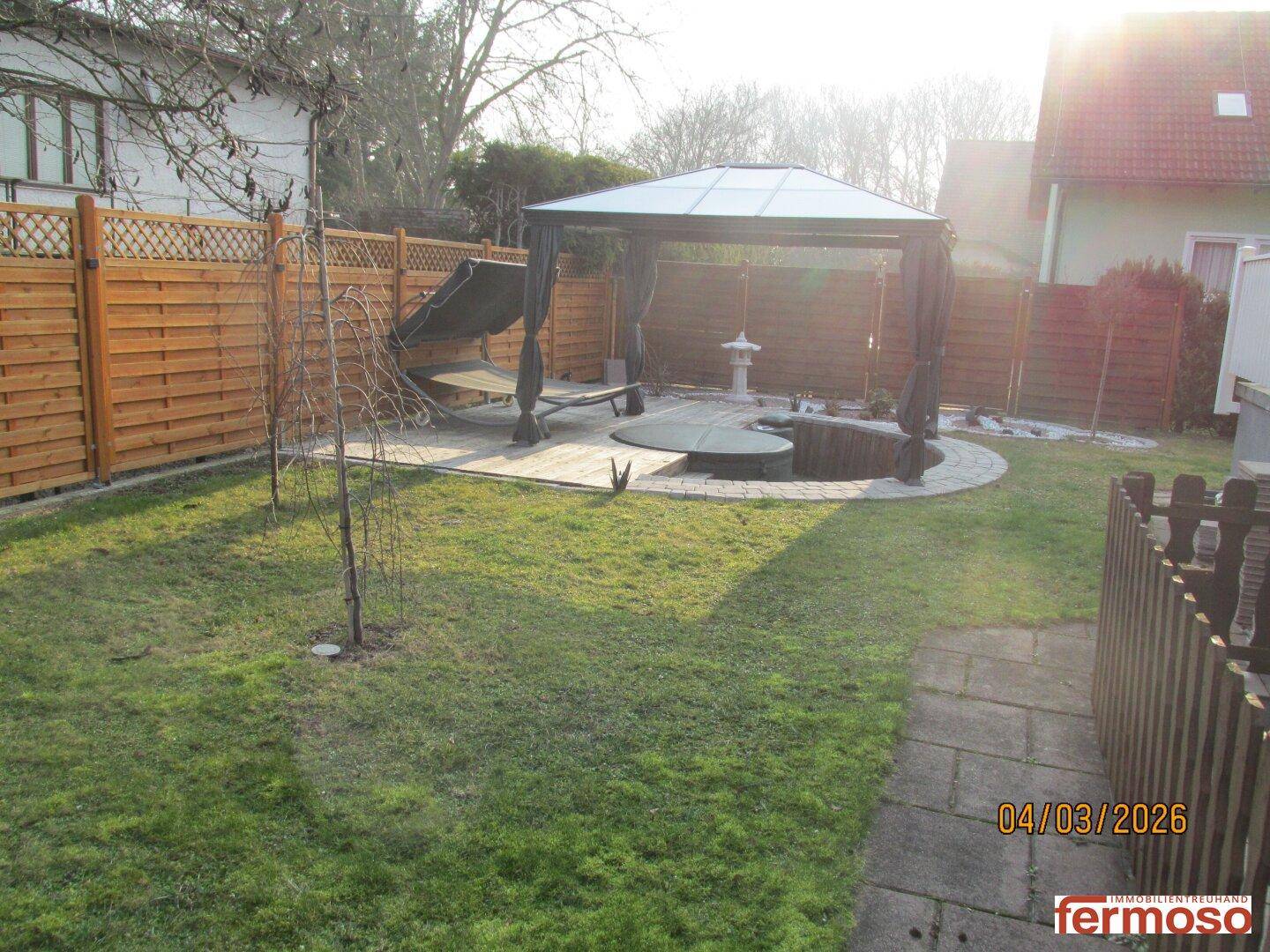 Sonniger Gartenbereich mit Rasen, Pavillon und Holzdeck, ideal für Entspannung im Freien.