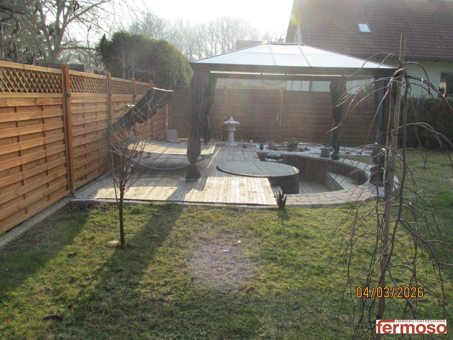 Sonniger Gartenbereich mit Rasen, Pavillon und Holzdeck, ideal für Entspannung im Freien.