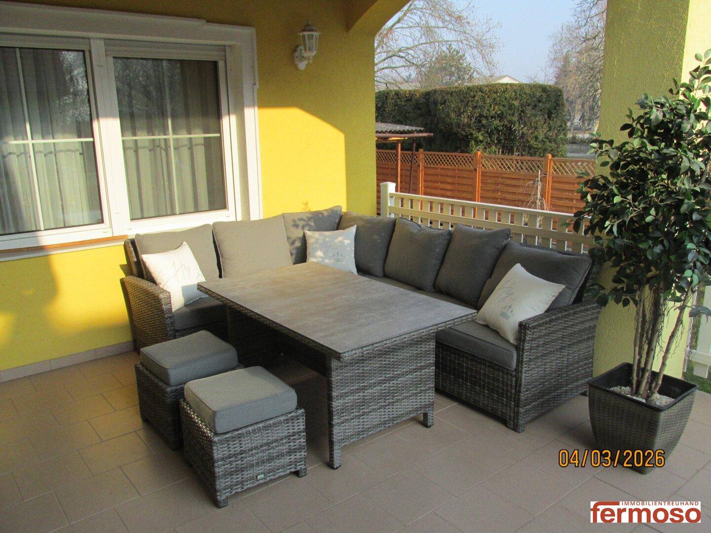 Gemütliche Terrasse mit Rattan-Sitzgruppe und Topfpflanze, ideal zum Entspannen im Freien.