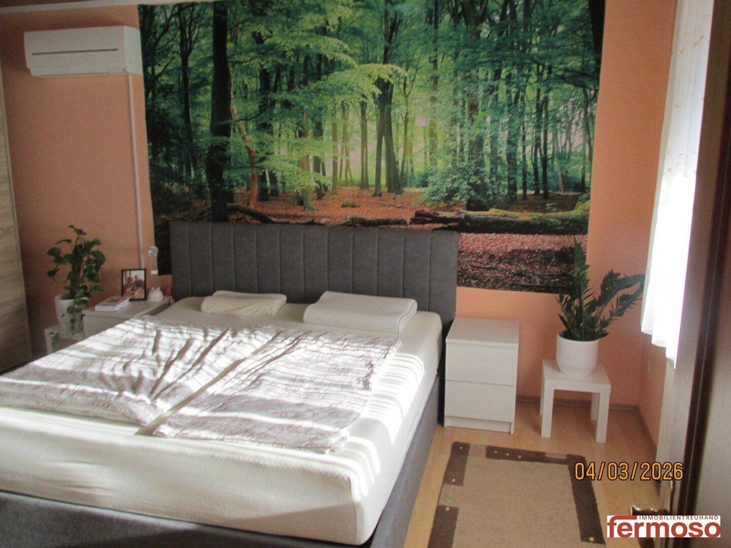 Gemütliches Schlafzimmer mit großem Bett, Nachttischen und einer Wanddekoration mit Waldmotiv.