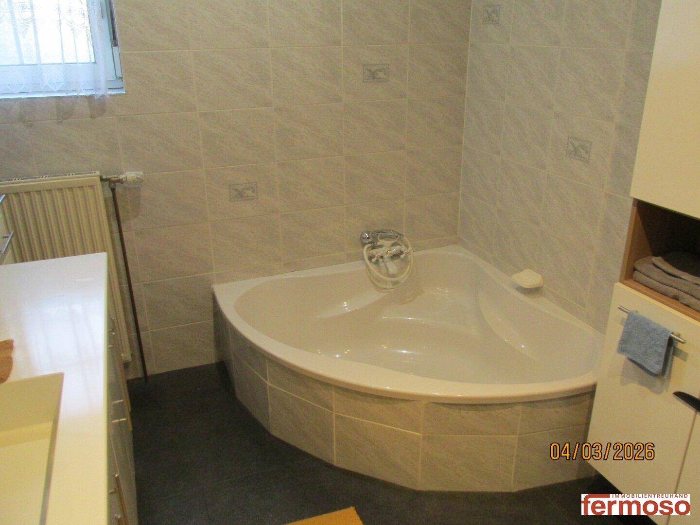 Badezimmer mit Eckbadewanne, Fliesenboden und Heizkörper, in hellem und funktionalem Design.