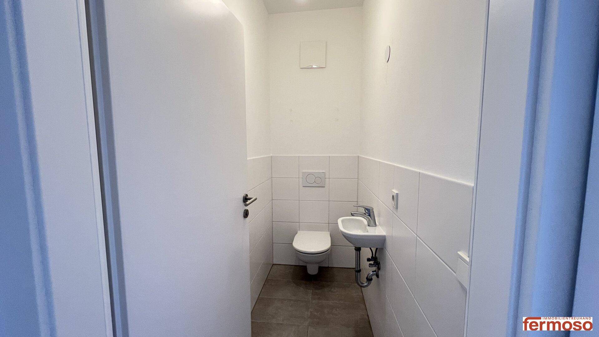 Kleines Gäste-WC mit Wand-WC, Waschbecken und weißen Fliesen, funktional und hell.