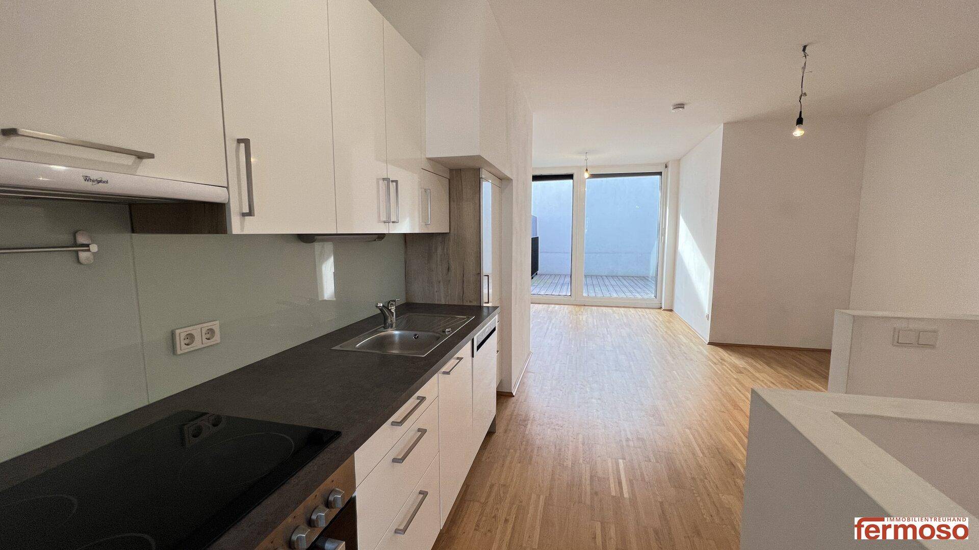 Moderne Einbauküche mit weißen Schränken und dunkler Arbeitsplatte, offen zum Wohnbereich mit Holzboden.