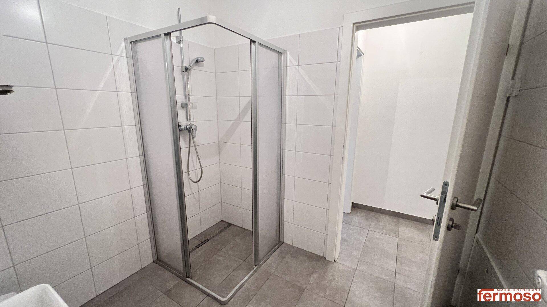Modernes Badezimmer mit Duschkabine, weißen Fliesen und dunklem Fliesenboden, funktional und sauber.