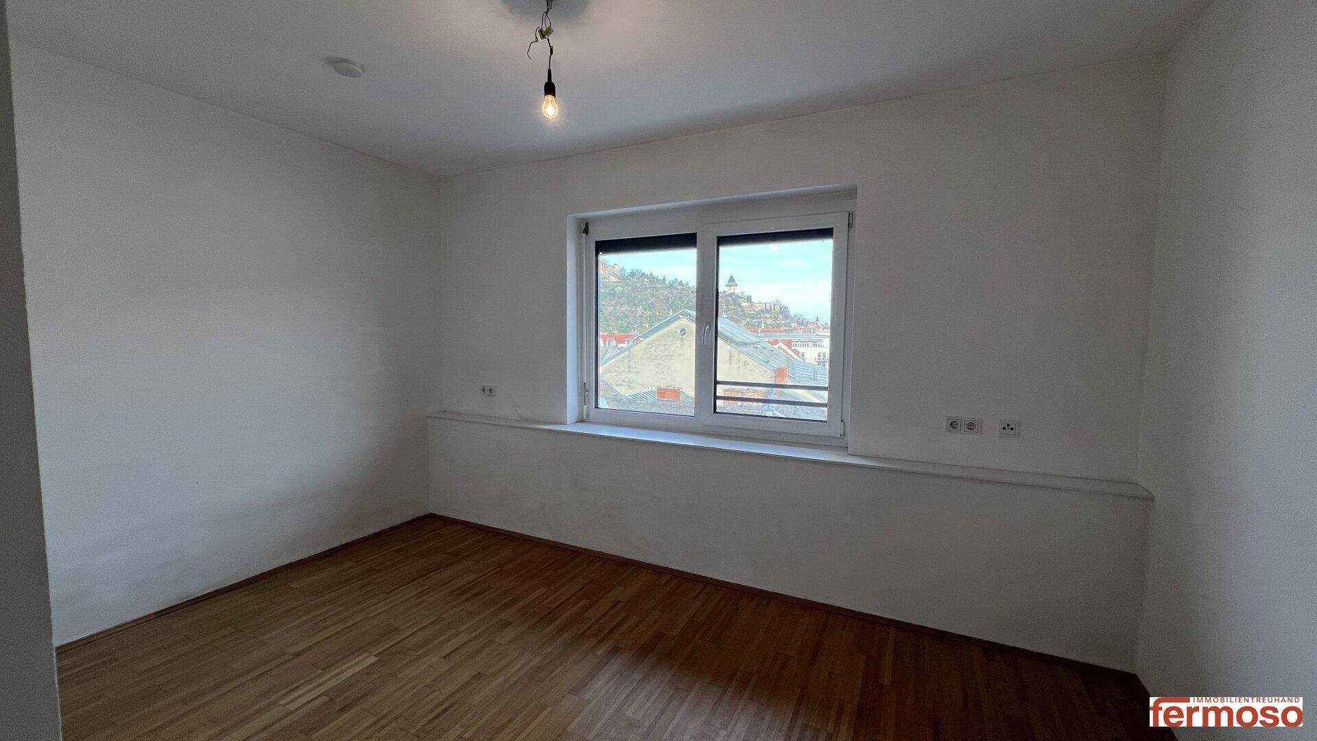 Geräumiges Schlafzimmer mit Holzboden und einem Fenster, das einen Blick auf die Umgebung bietet.