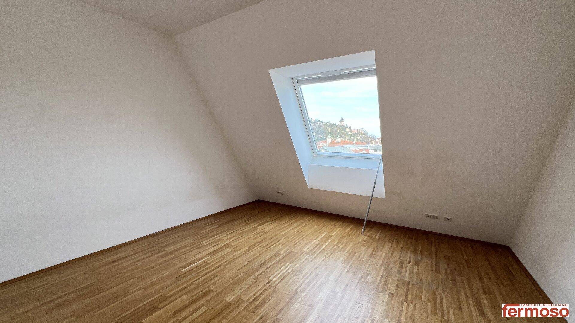 Helles Schlafzimmer im Dachgeschoss mit schrägen Wänden, Holzboden und einem großen Dachfenster.