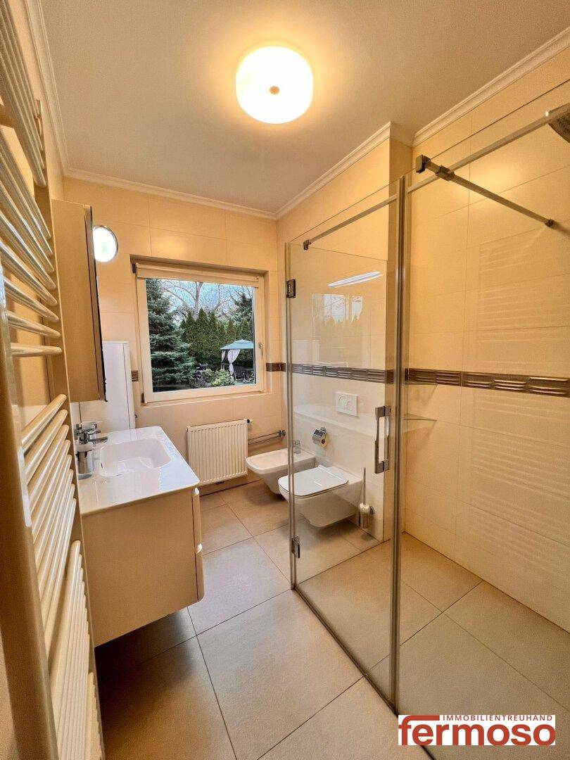 Helles Badezimmer mit Fenster, begehbarer Dusche, WC, Bidet und Blick ins Grüne.