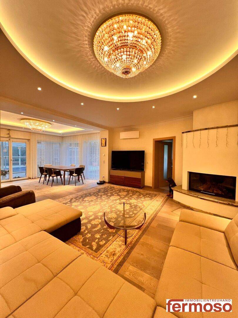 Eleganter Wohnbereich mit großem Kronleuchter, gemütlichem Sofa und integriertem Essbereich.