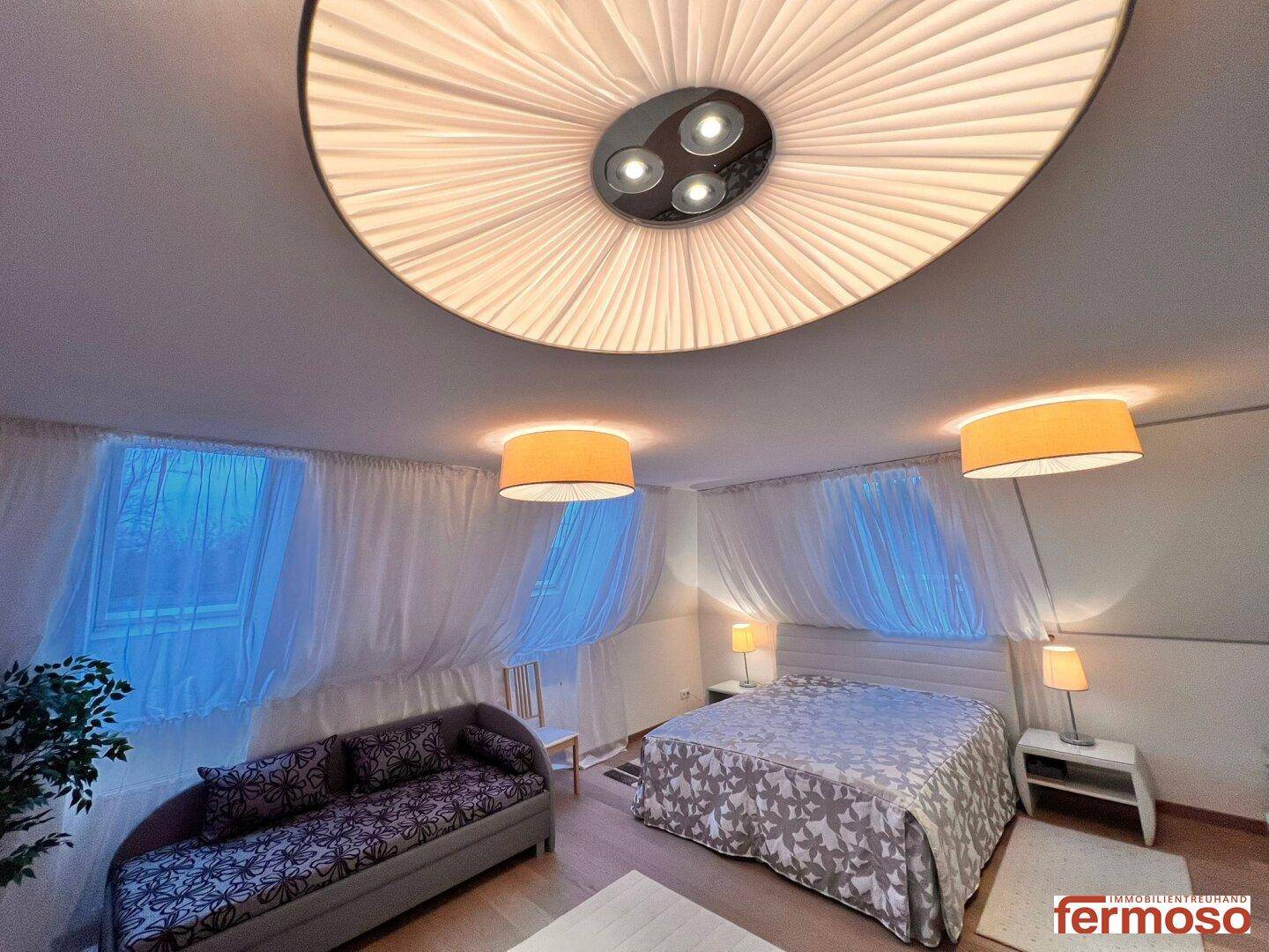 Gemütliches Schlafzimmer mit Doppelbett, Sofa und auffälliger Deckenleuchte.