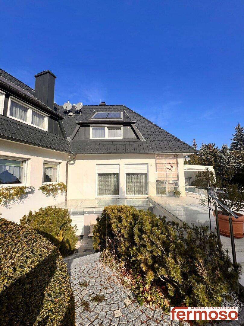 Elegante Hausfassade mit dunklem Dach, weißen Wänden und gepflegter Außenanlage.