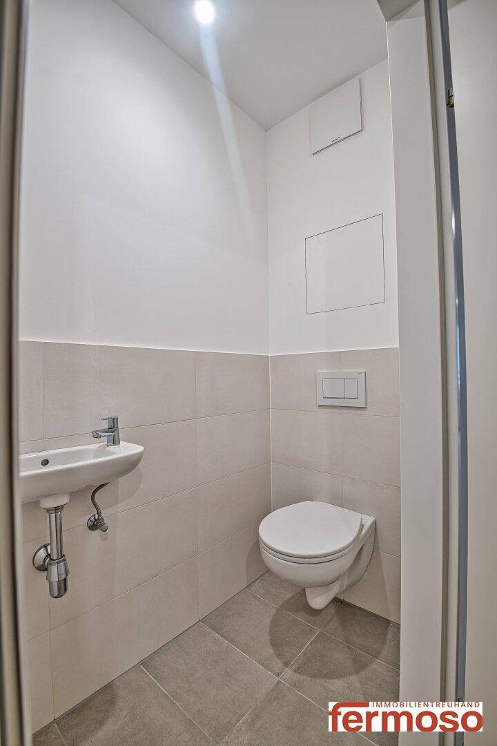 Modernes Gäste-WC mit Wand-WC, kleinem Waschbecken und hellen Fliesen.