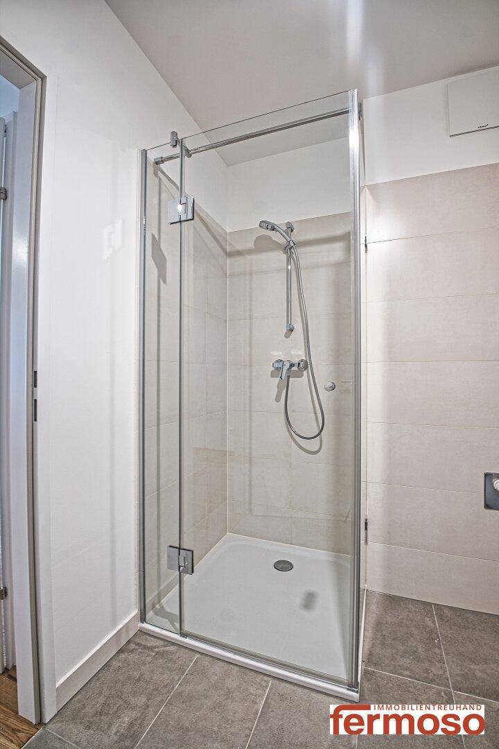 Modernes Badezimmer mit Duschkabine, hellen Fliesen und minimalistischem Design.