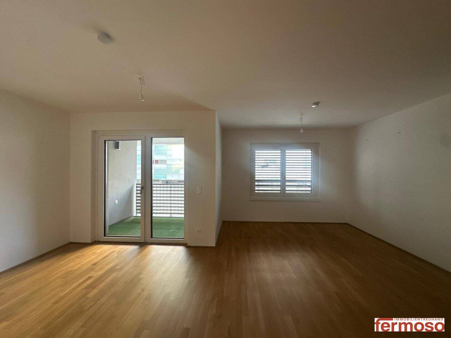 Geräumiger, heller Wohnbereich mit Parkettboden und großem Fenster mit Zugang zum Balkon.