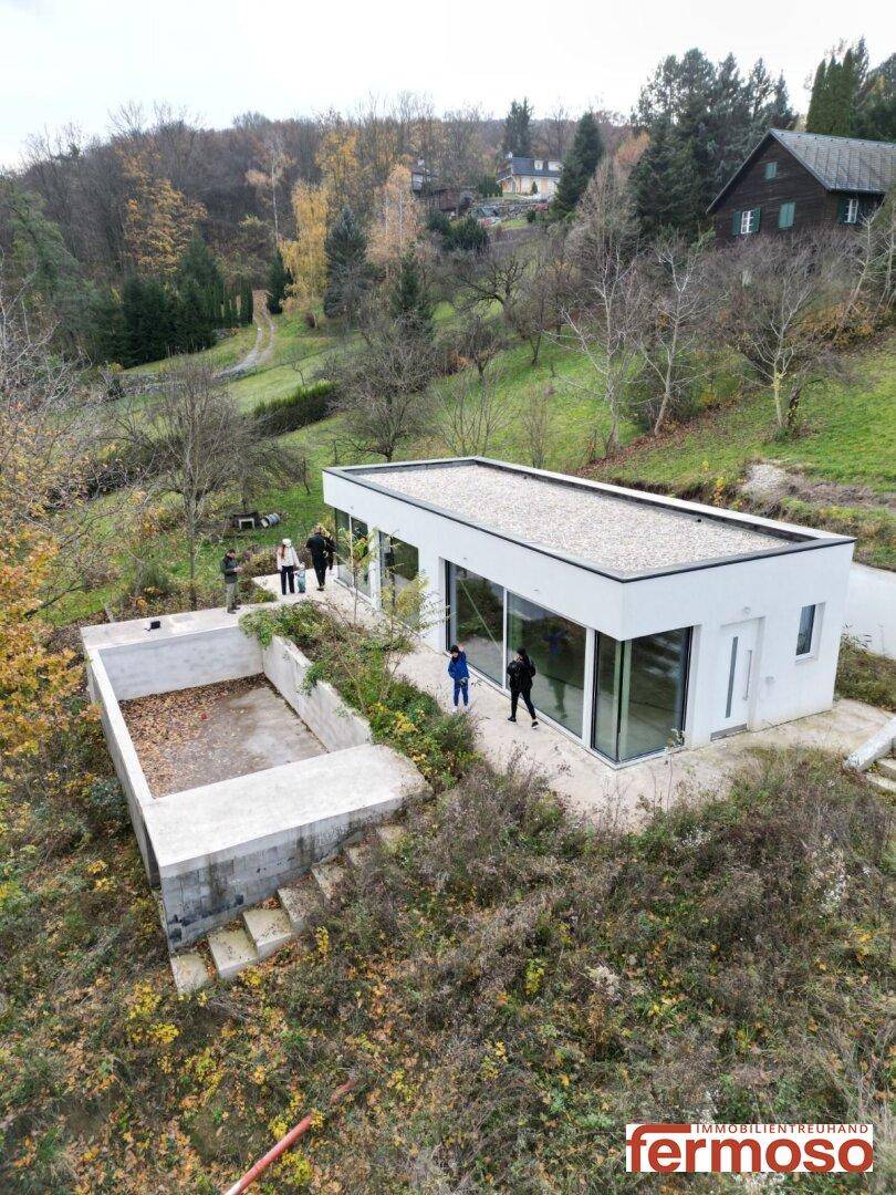 Luftaufnahme des modernen Hauses mit unfertigem Poolbereich, eingebettet in eine grüne Hügellandschaft.