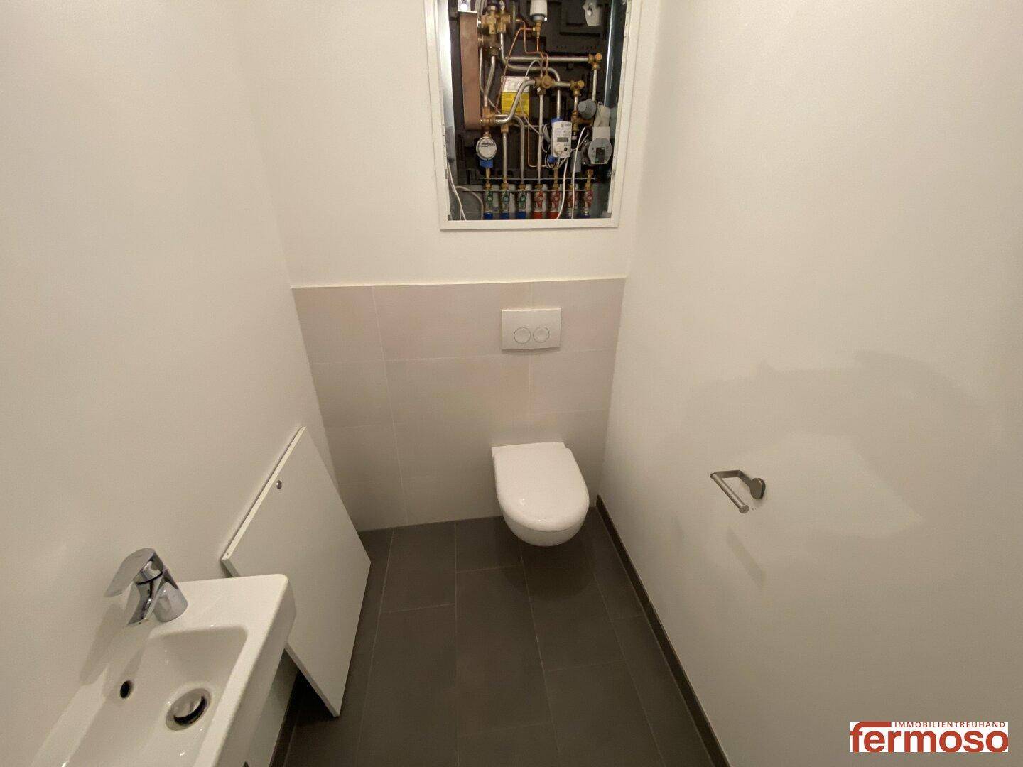 Modernes Gäste-WC mit Wand-WC, kleinem Waschbecken und dunklen Bodenfliesen.