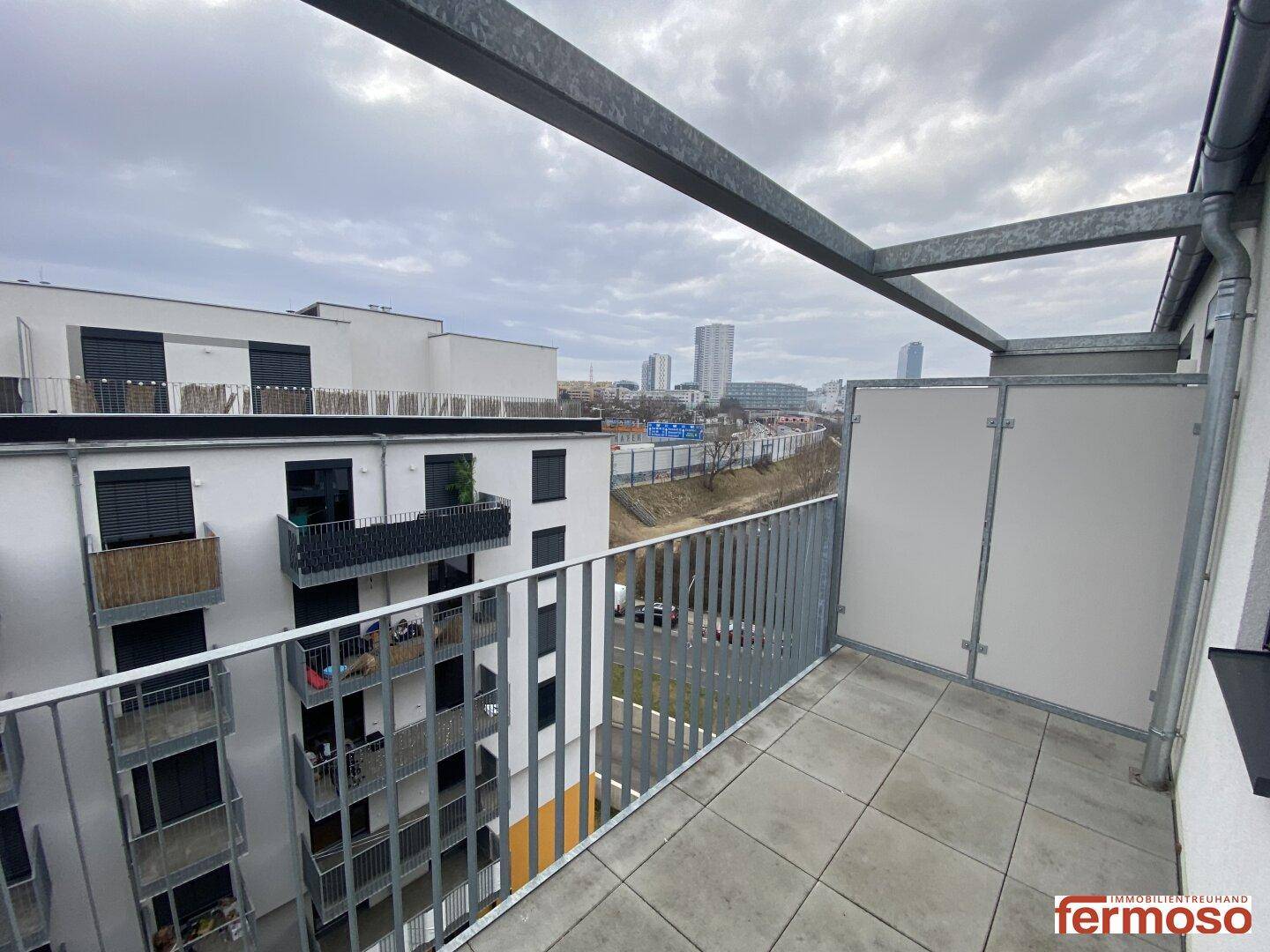 Geräumiger Balkon mit Fliesenboden und Blick auf die Stadt und umliegende Gebäude.