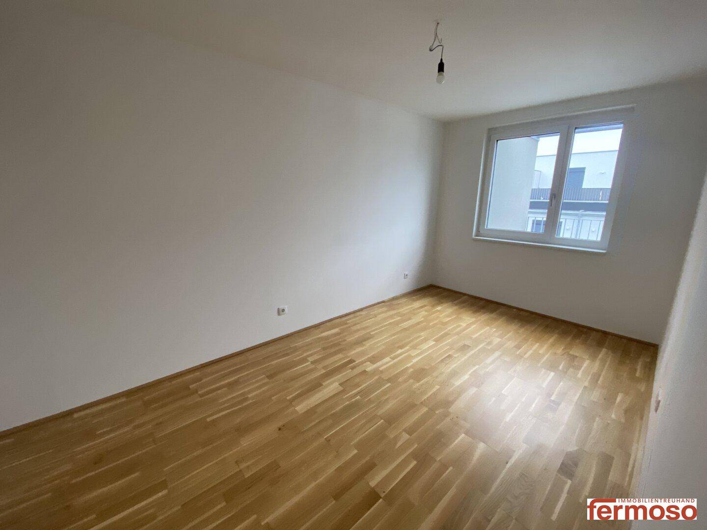 Unmöbliertes Schlafzimmer mit hellem Parkettboden und einem großen Fenster für viel Tageslicht.