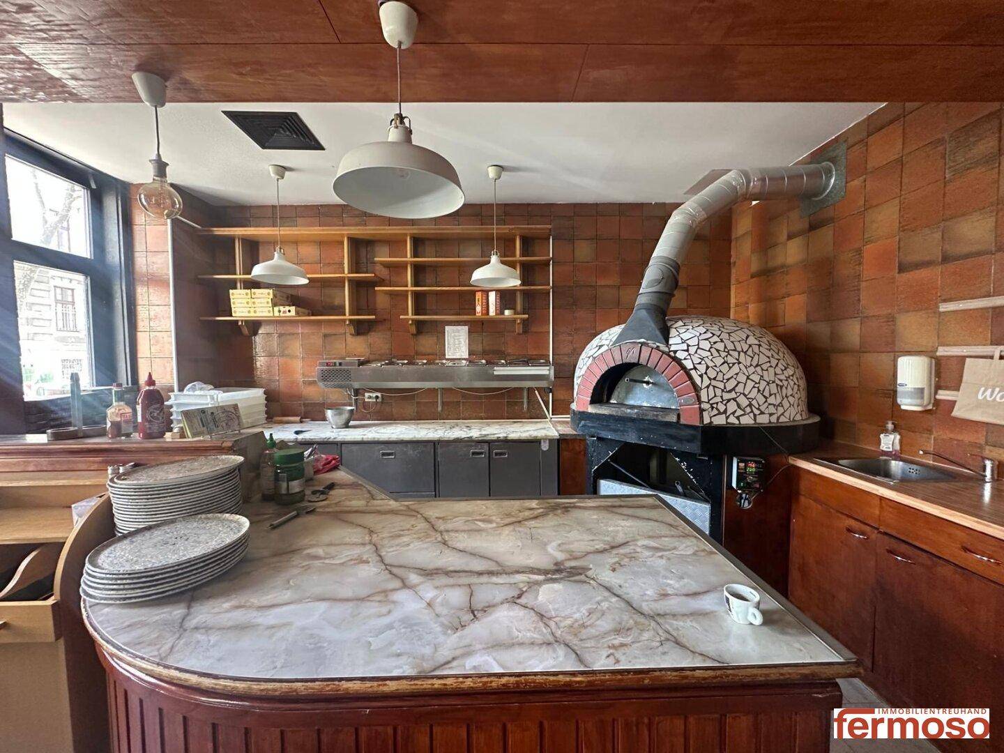 Professionelle Restaurantküche mit großem Pizzaofen, Marmorarbeitsplatte und Fliesenwänden.