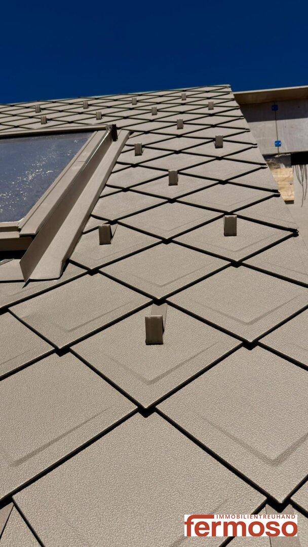 Detailaufnahme des Daches mit modernen Dachziegeln und Dachfenster während der Bauphase.