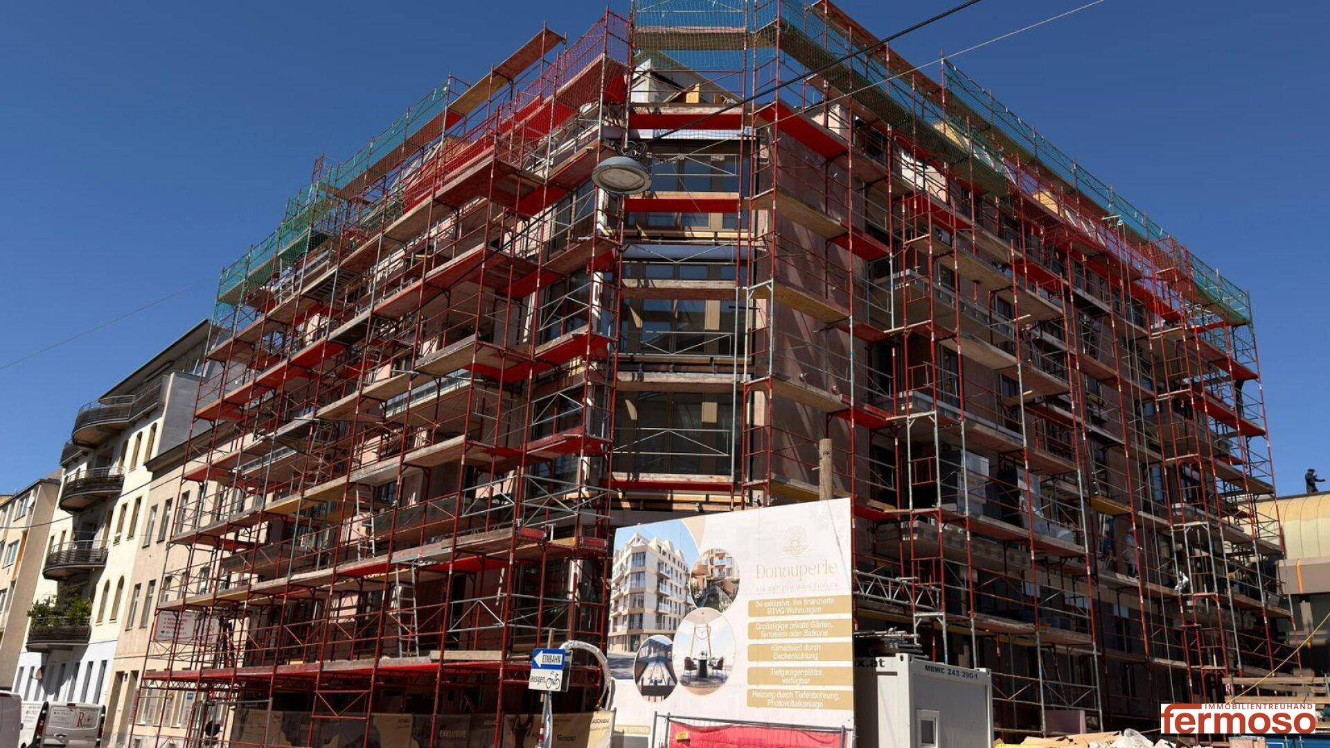 Neubau-Wohngebäude mit Gerüst und Bauplakat an einem sonnigen Tag.