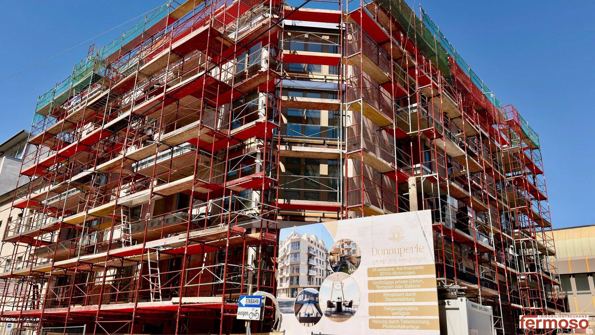 Neubau-Wohngebäude mit Gerüst und Bauplakat an einem sonnigen Tag.