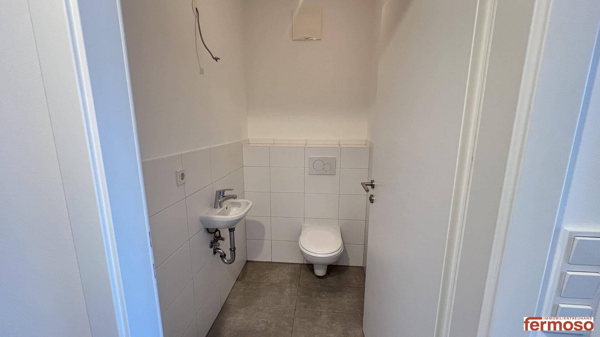 Separates Gäste-WC mit Waschbecken, Toilette und weißen Wandfliesen.