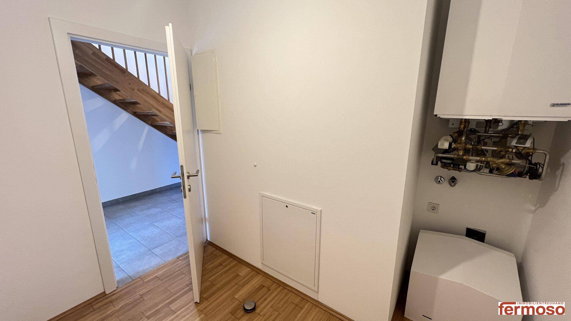 Flur mit Heizungsanlage und Zugang zu den oberen Etagen über eine Holztreppe.