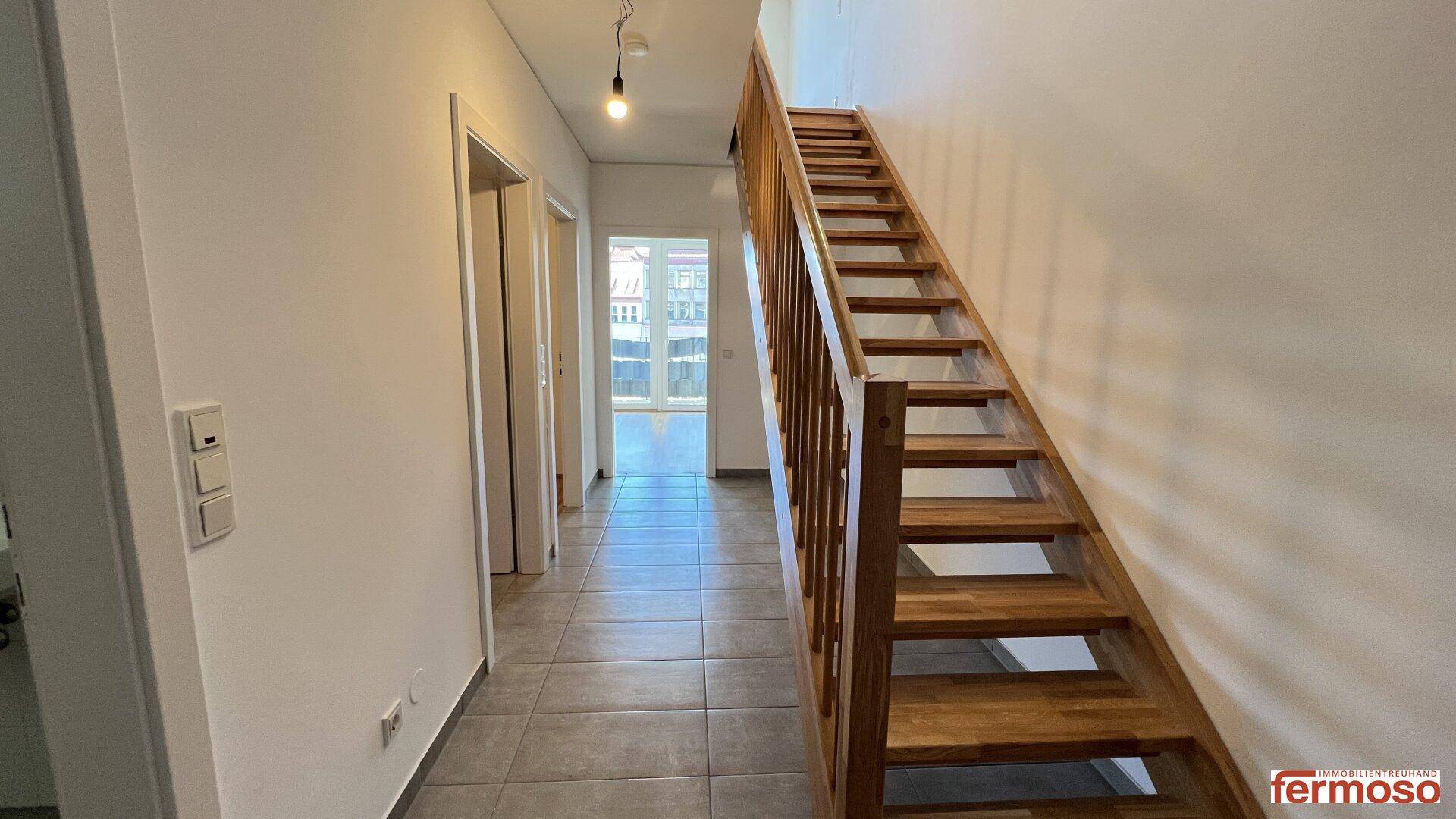 Heller Flur mit Fliesenboden und einer eleganten Holztreppe zu den oberen Etagen.