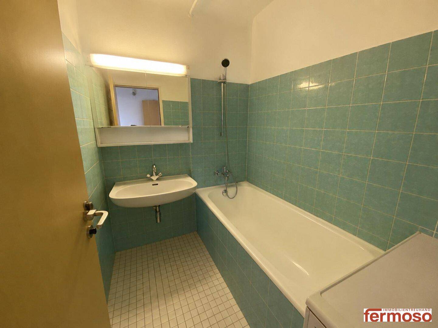 Badezimmer mit Badewanne, Waschbecken und hellblauen Fliesen im Retro-Stil.