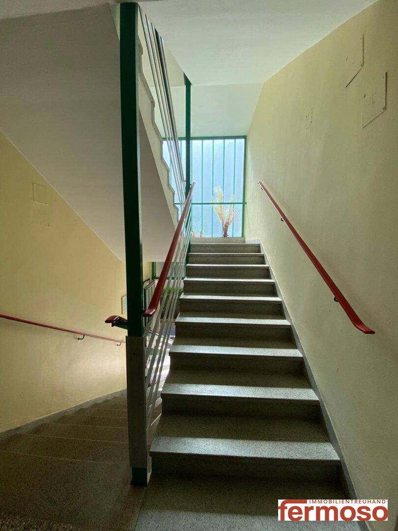 Treppenhaus mit mehreren Etagen, Geländer und Fenstern für natürliches Licht.