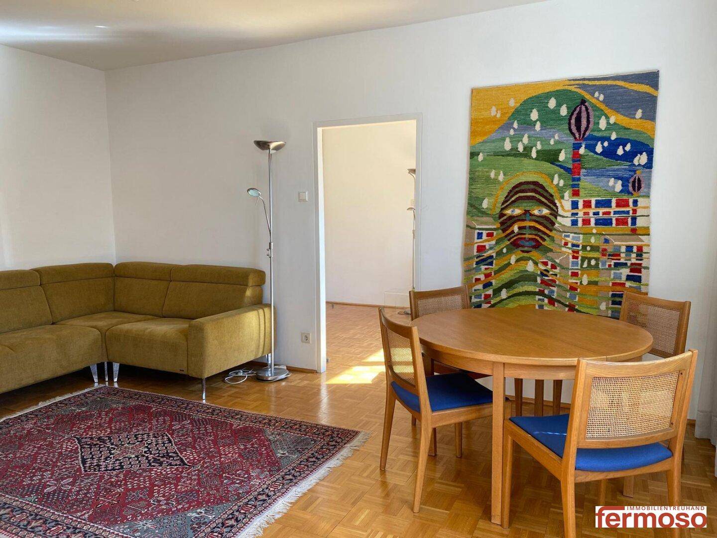 Gemütlicher Wohn- und Essbereich mit Parkettboden, Ecksofa und einem großen Wandteppich.