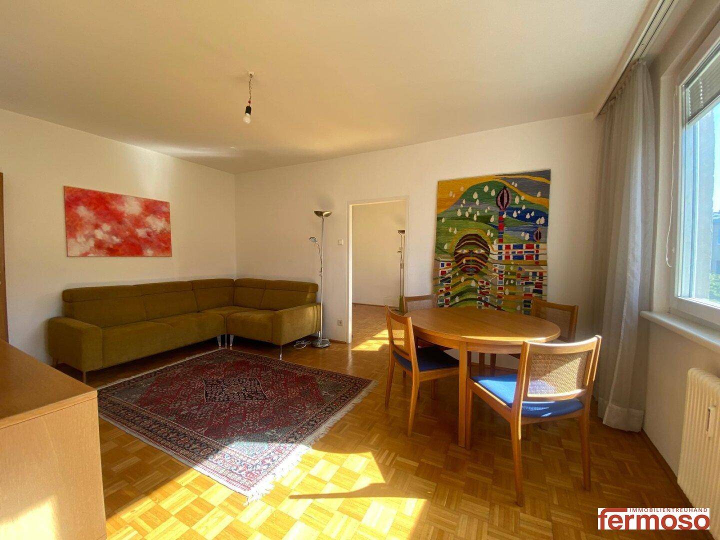 Heller Wohn- und Essbereich mit Parkettboden, Ecksofa und Kunstwerken an den Wänden.