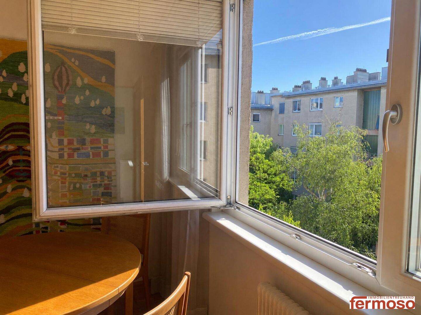 Heller Essbereich mit Holztisch und Blick ins Grüne auf die umliegenden Gebäude.