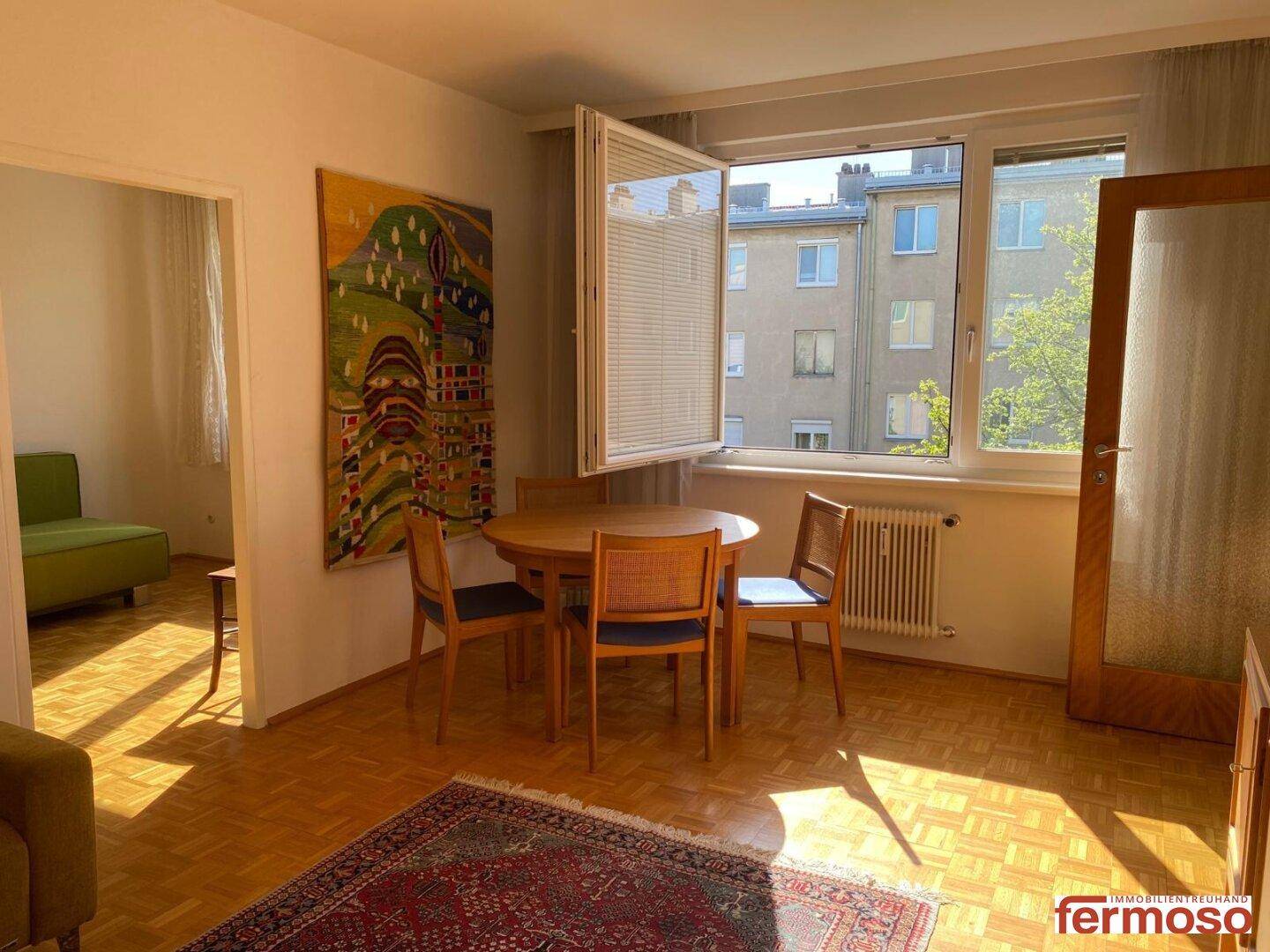 Geräumiger Wohn- und Essbereich mit Parkettboden, gemütlichem Sofa und farbenfrohem Teppich.