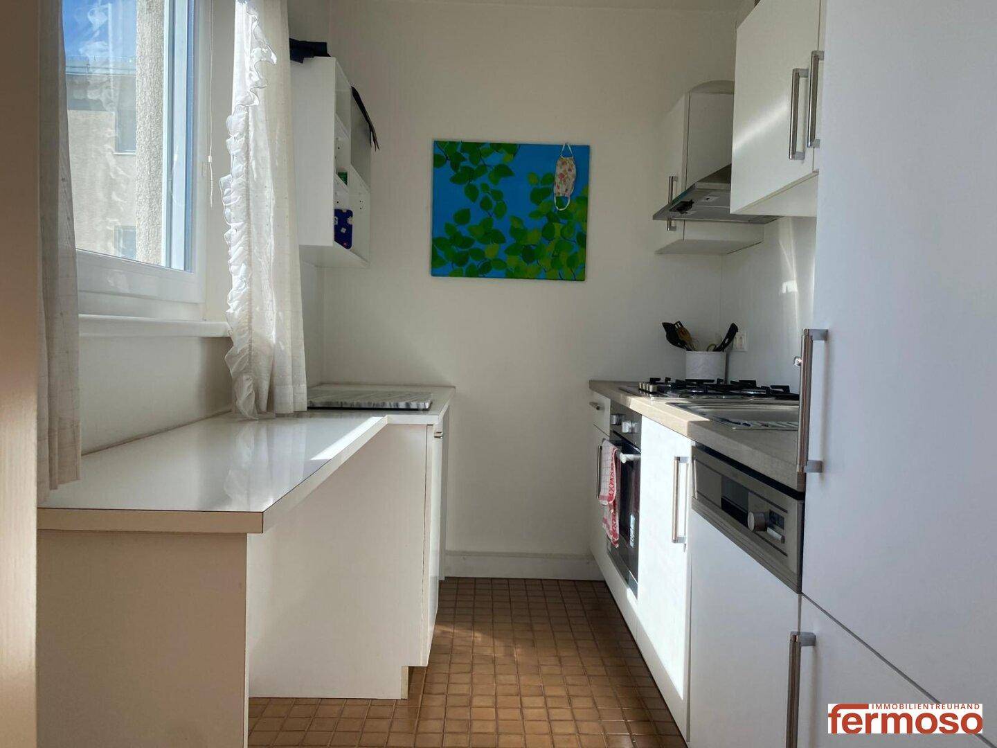 Helle Küche mit weißen Einbauschränken, Fenster und praktischer Arbeitsfläche.