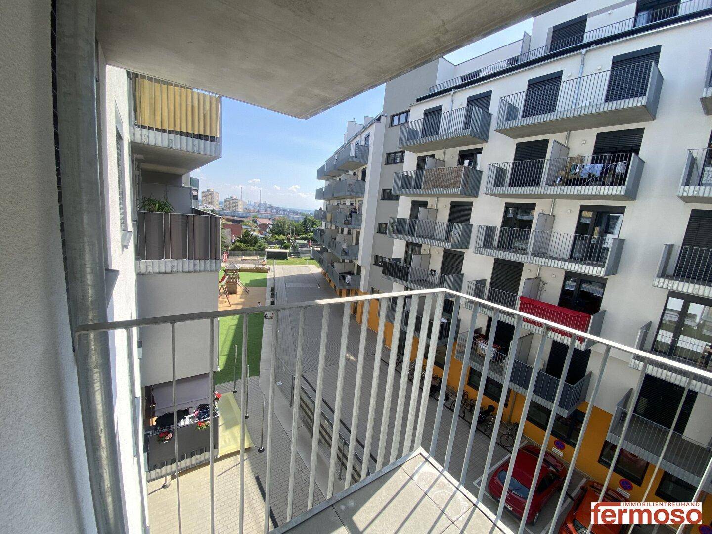 Blick vom Balkon auf den Innenhof mit Spielplatz und umliegenden Wohngebäuden.