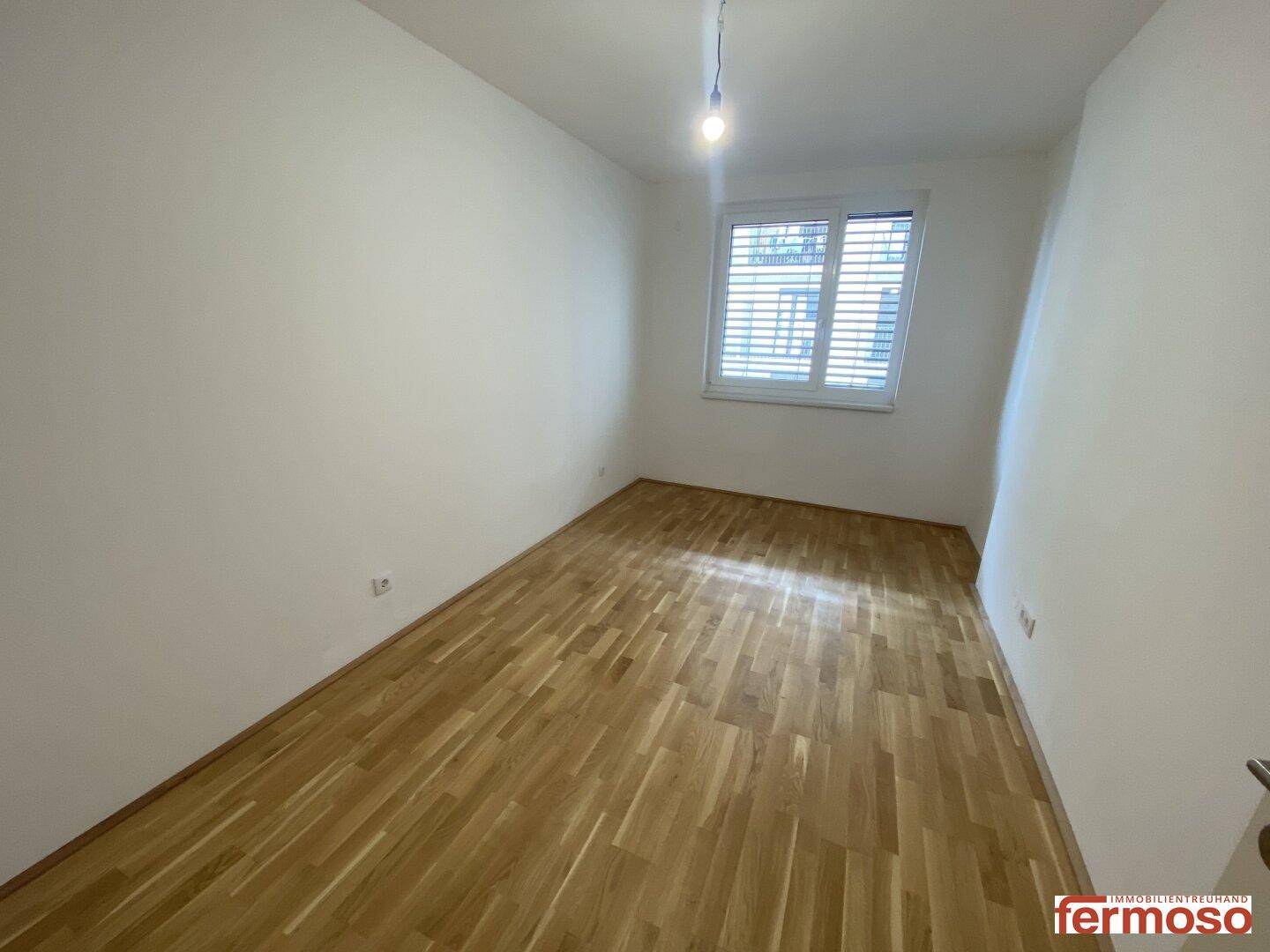 Helles Schlafzimmer mit Holzboden und Fenster, das viel Tageslicht hereinlässt.