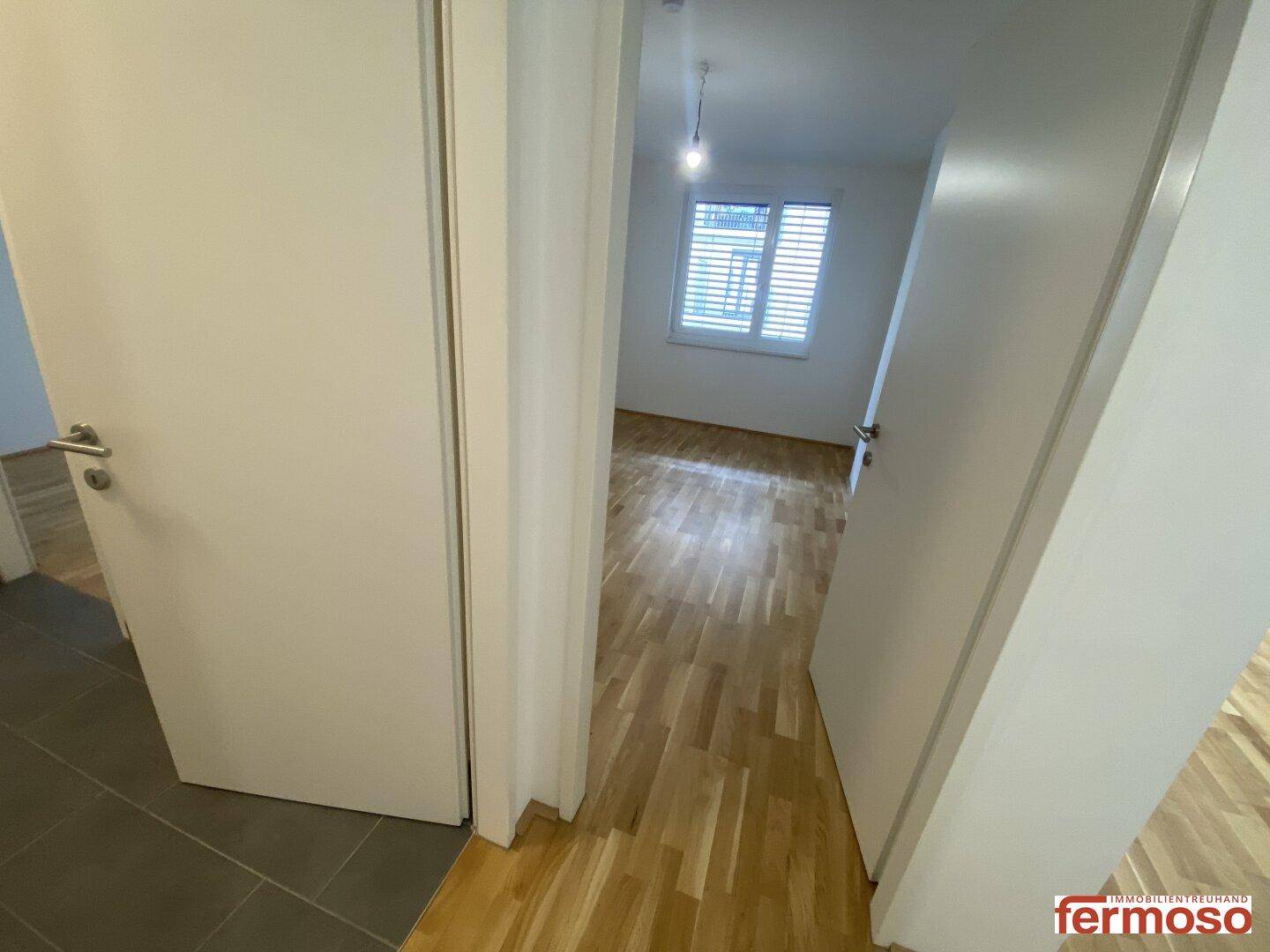 Heller Flur mit Parkettboden, der zu einem weiteren Zimmer mit Fenster führt.