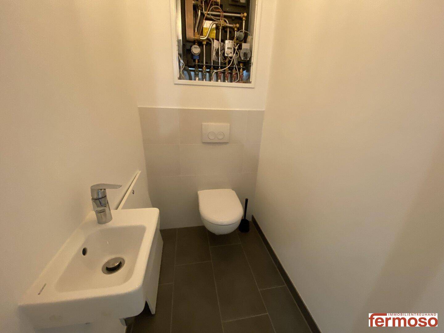 Separates WC mit wandhängender Toilette und kleinem Waschbecken, modern gefliest.