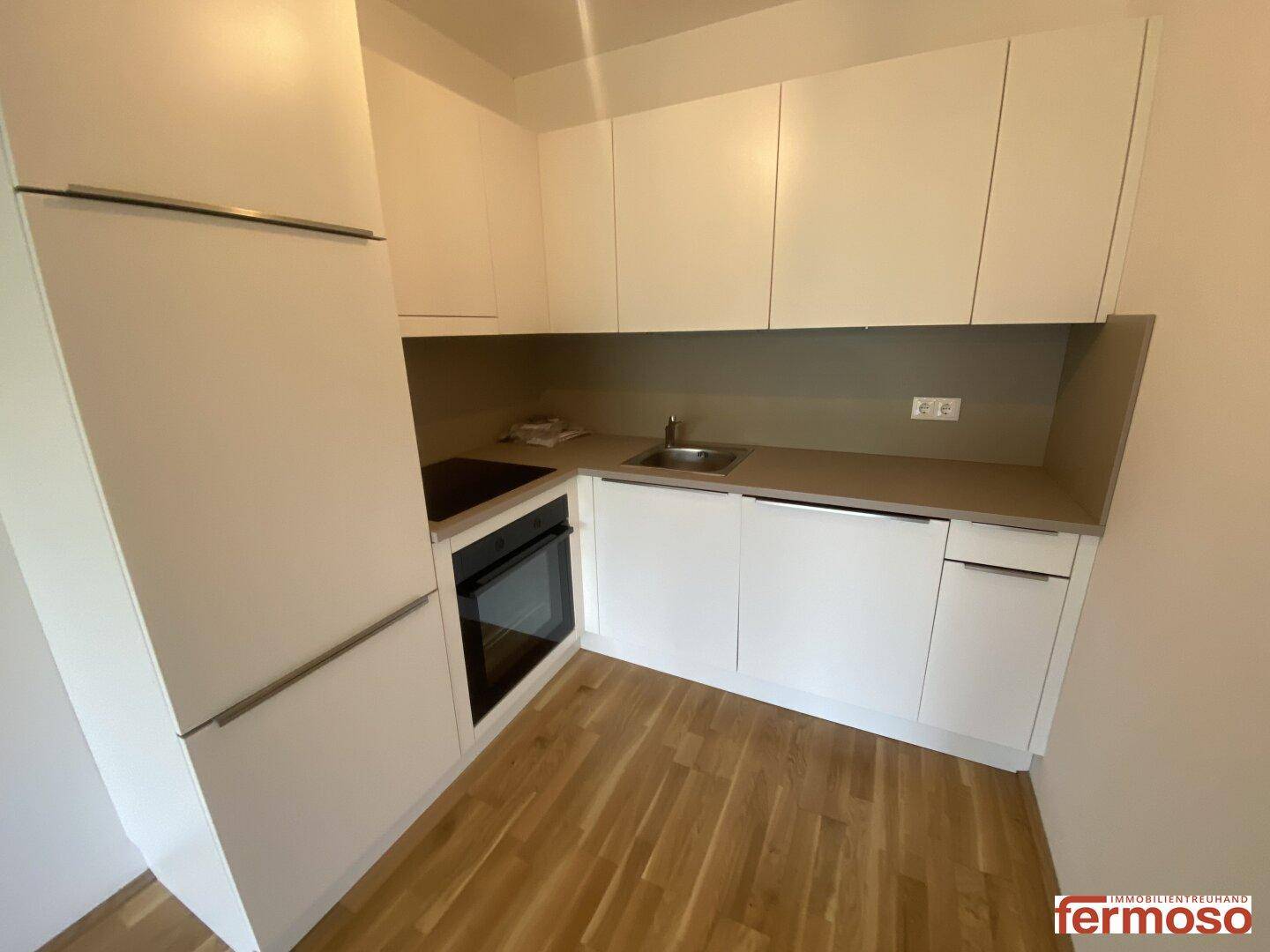 Moderne Einbauküche mit weißen Schränken, integrierten Geräten und hellem Parkettboden.