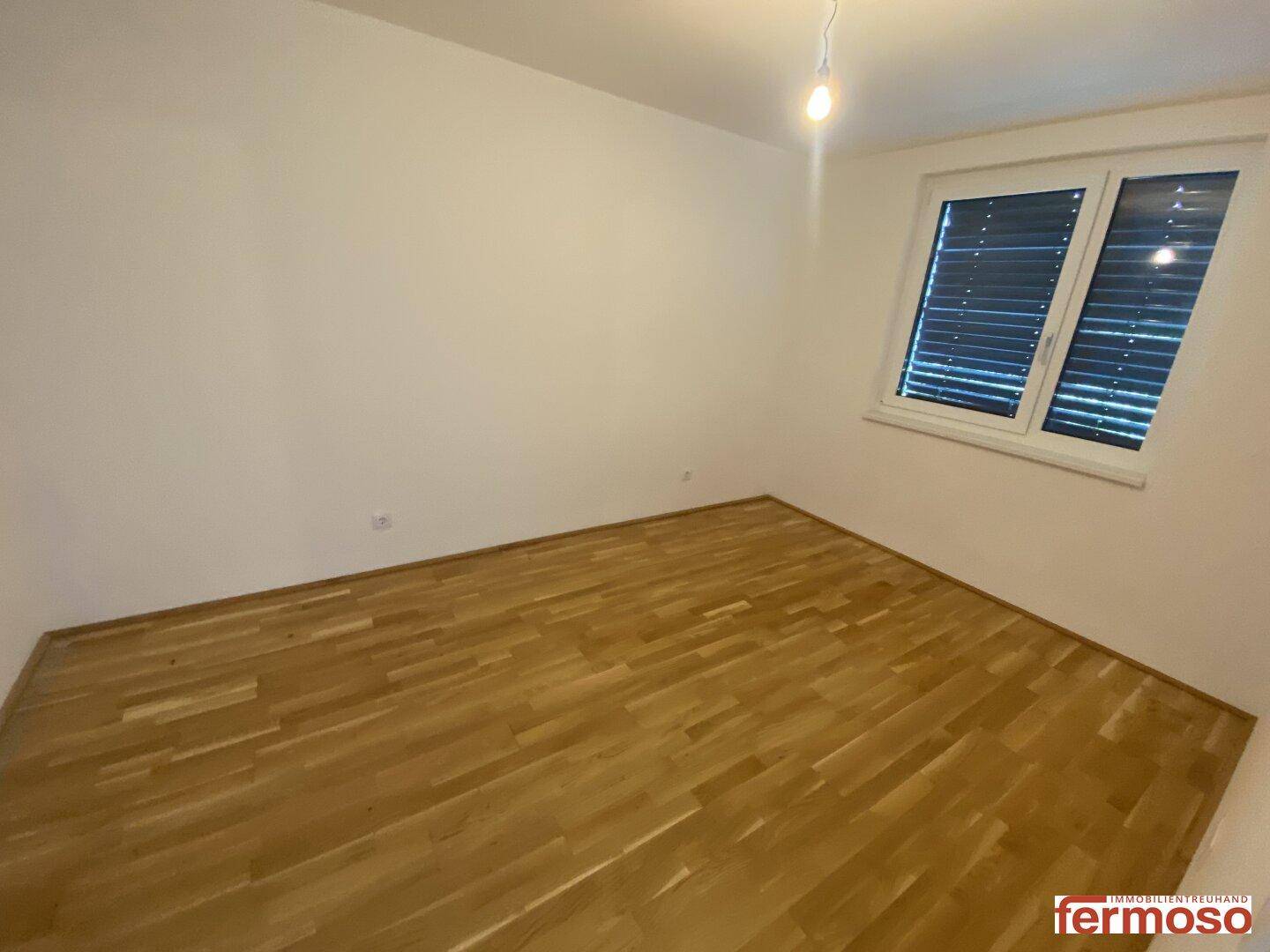 Helles Zimmer mit Parkettboden und Fenster, bereit zur individuellen Gestaltung.