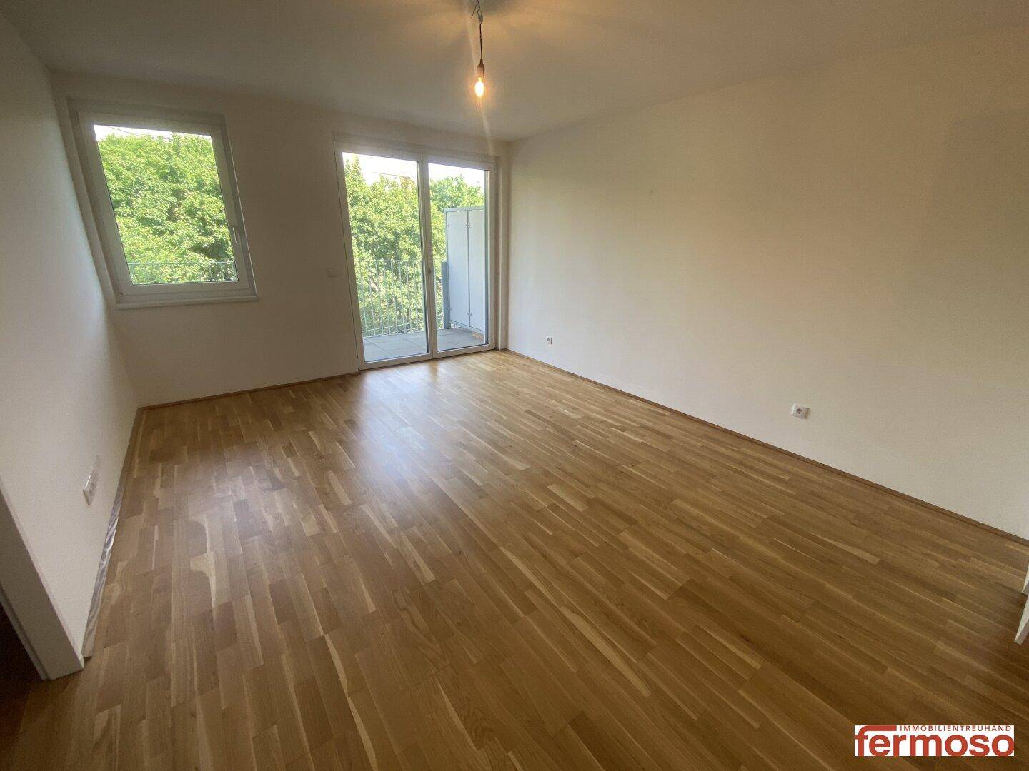Geräumiges Wohnzimmer mit Parkettboden, großen Fenstern und Zugang zum Balkon.