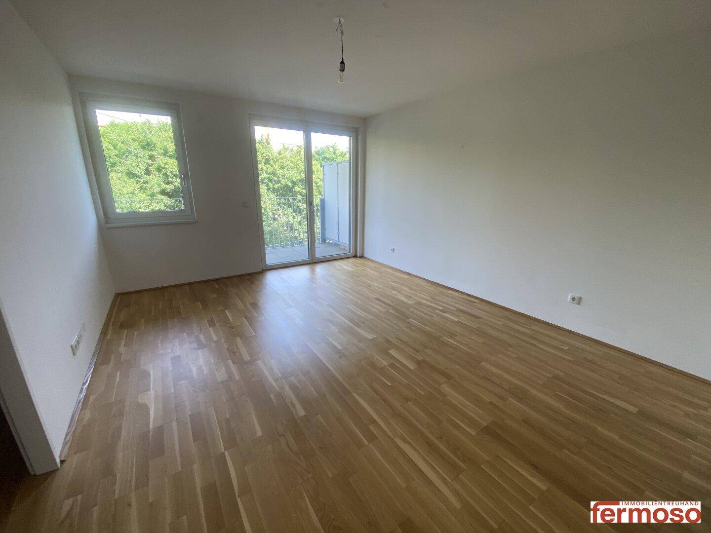 Heller Wohnbereich mit Parkettboden und breiter Balkontür, bietet viel Tageslicht und Ausblick.