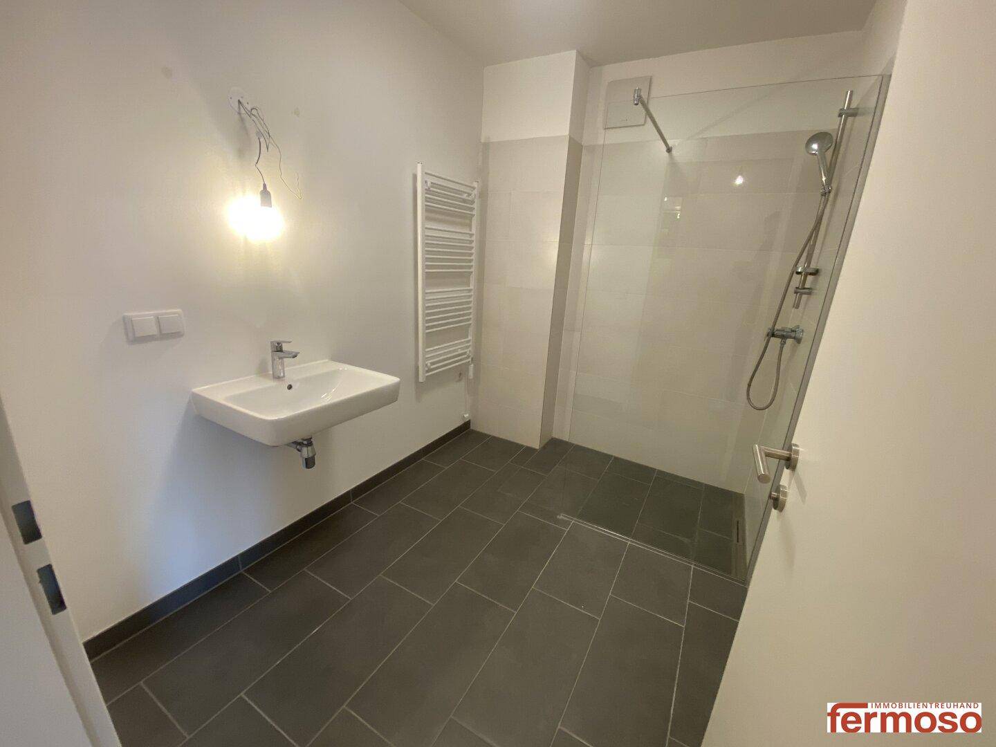 Modernes Badezimmer mit ebenerdiger Dusche, Waschbecken und beheiztem Handtuchhalter.
