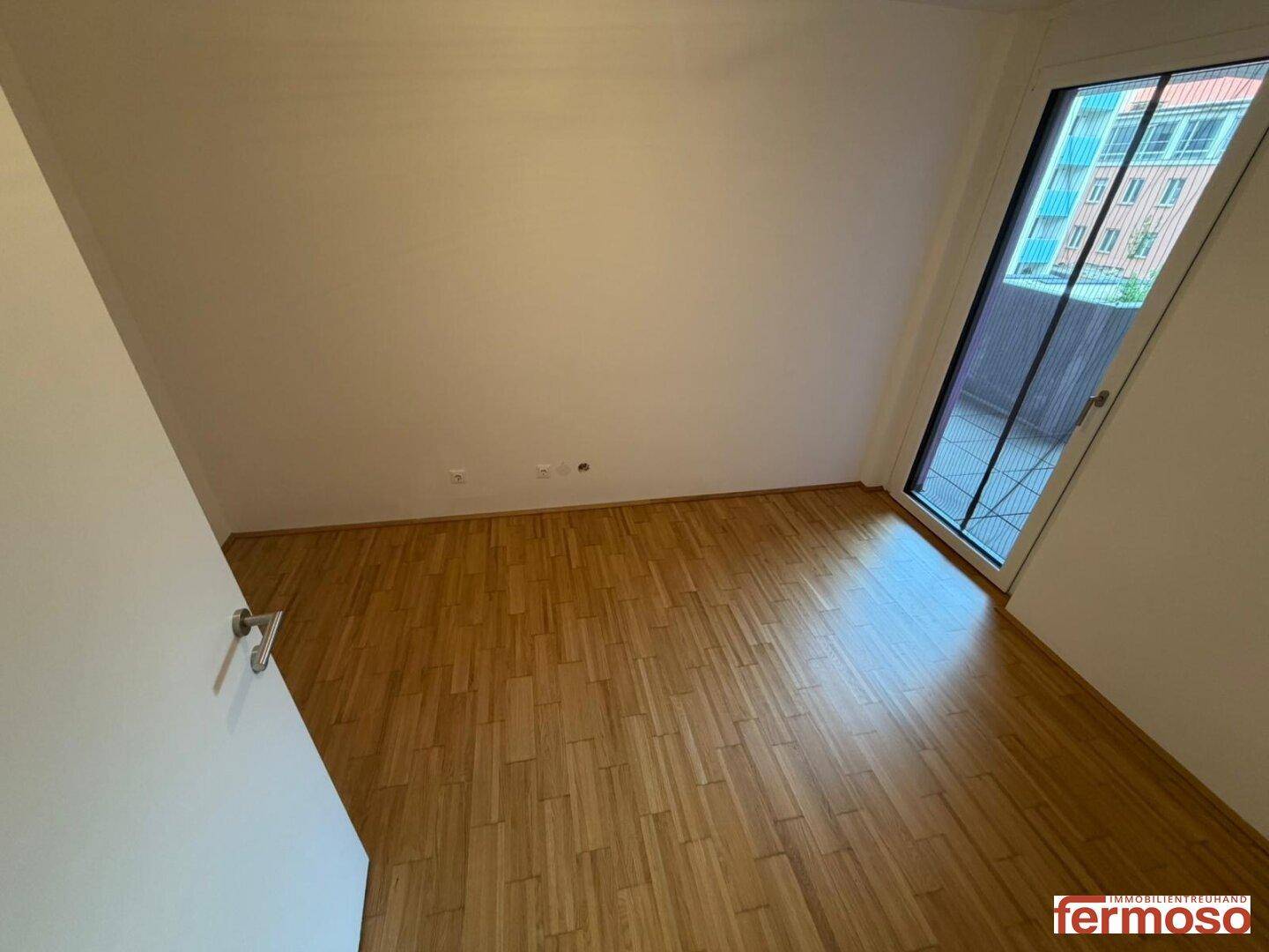 Helles Schlafzimmer mit Holzboden und großen Fenstern zum Balkon, ideal für viel Tageslicht.