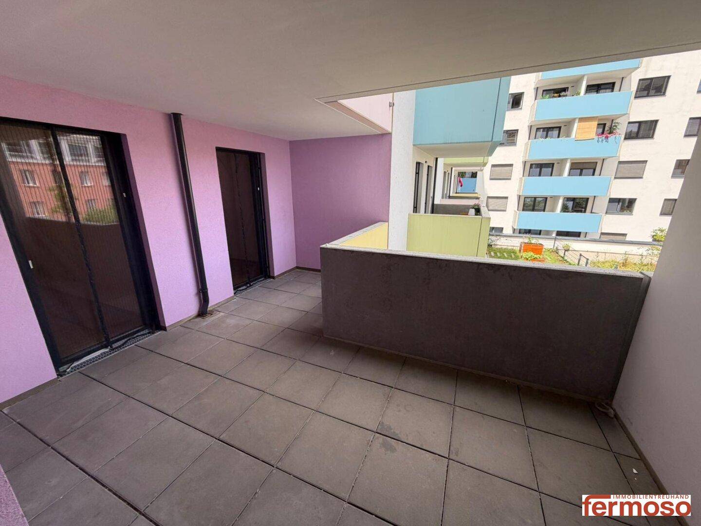 Geräumiger Balkon mit Fliesenboden und farbigen Wänden, bietet Blick auf umliegende Gebäude.