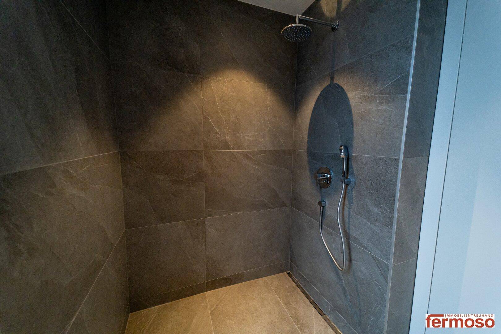 Moderne Duschkabine mit großformatigen grauen Fliesen und Regendusche.