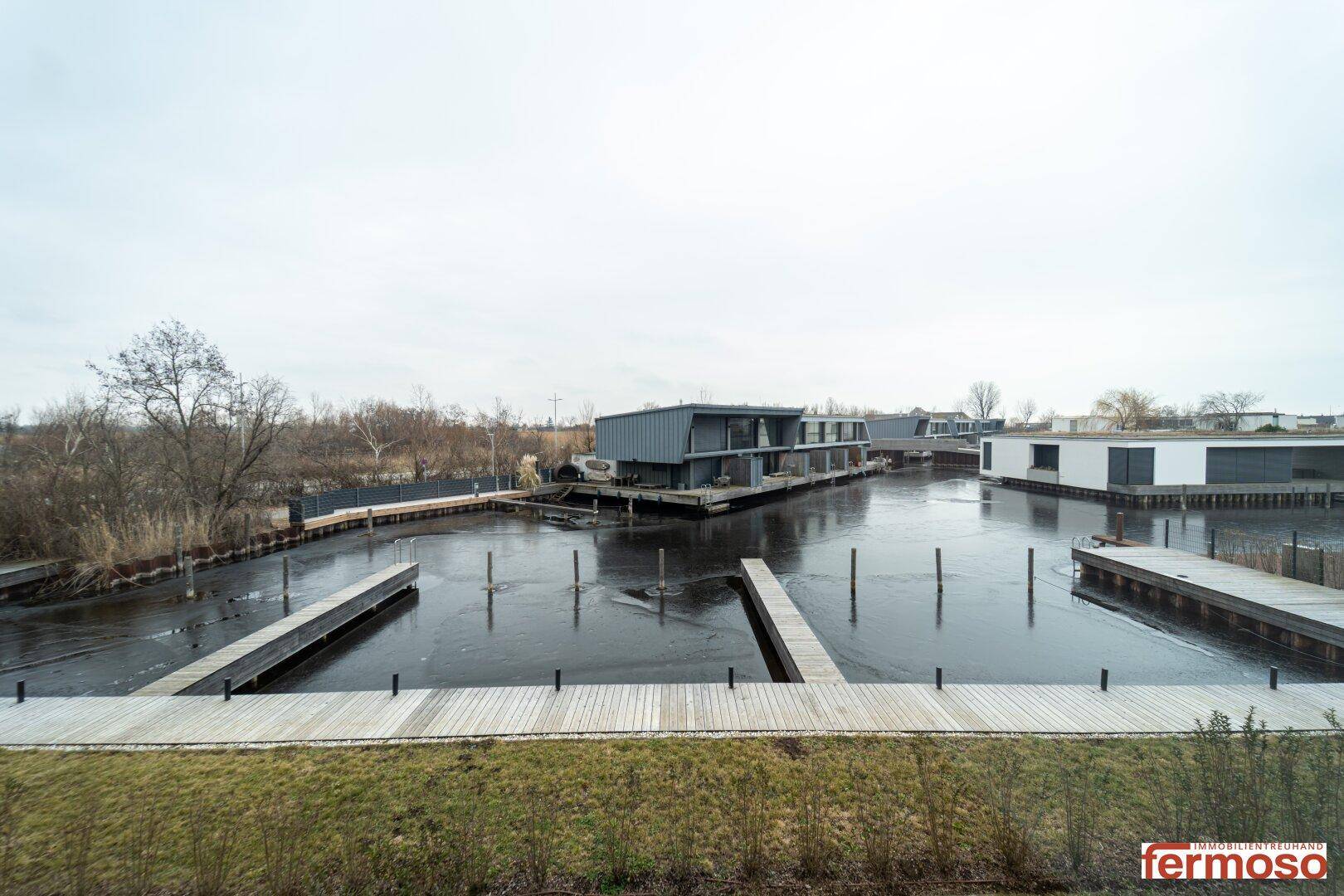 Blick auf die gefrorene Marina mit Bootsstegen und modernen Häusern im Hintergrund.